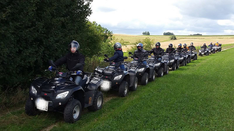 11 schwaze Quads in Kolonne auf einem Feldweg