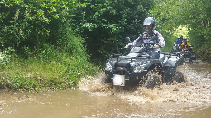 Ein Quadfahrer fährt durch den Fluss mit seinem grünen Quad