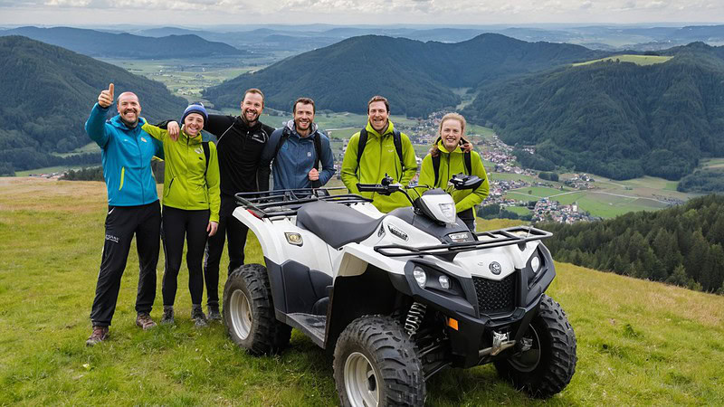 6 Personen stehen um ein Quad, im Hintergrund weites, Bergiges Land