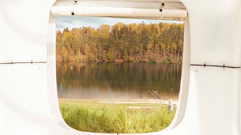 Ausgang des Sleep Cubes direkt zum See, perferkter Blick auf einen See mit Wald bei blauer Stujnde