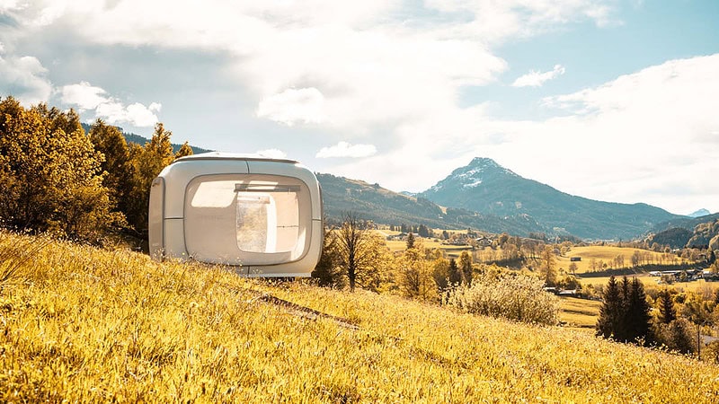 Aussicht auf den Sleep Cube und die Alpen von einem Hügel aus.