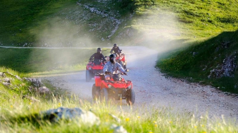 3 rote Quads auf einem Schotterweg zwischen Hügeln