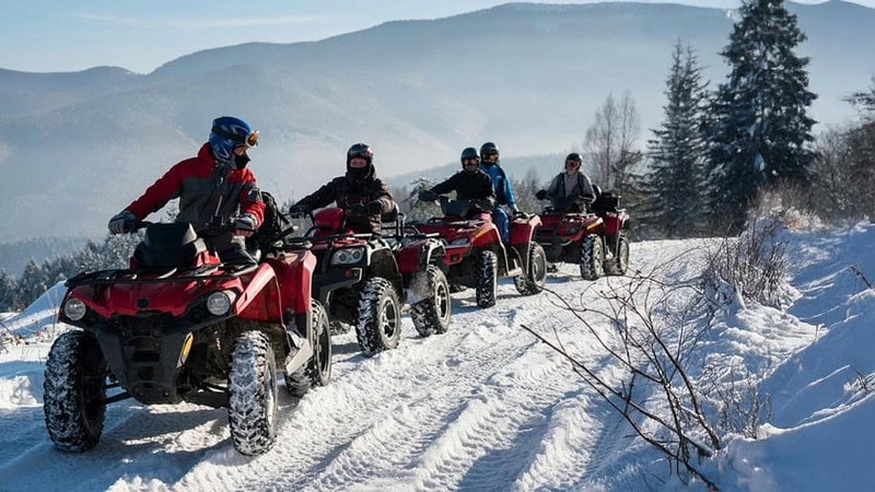 Eine Gruppe von Quadfahrern die hintereinander auf Schnee fahren.